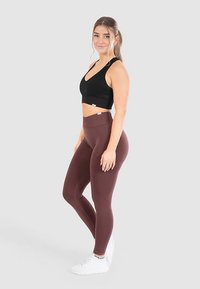 Zwart cropped sportbeha en high-waisted bordeauxrode leggings. Gladde stof, nauwsluitend ontwerp en contrasterende witte sneakersdetails.