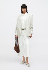 Leinenblazer in Hellbeige, weißes Hemd, weite weiße Hose, braune Handtasche und hellgraue Slipper. Schlichtes Design mit minimalen Akzenten.