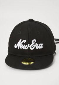 Svart åtsittande keps med vit "New Era" broderad på framsidan och guldfärgad storleksklistermärke på den platta skärmen, visas mot en enkel ljus bakgrund.