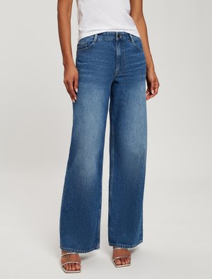 Wide-leg blue jeans made of denim, featuring a high waist, faded sections, and a clean hem. Paired with silver strappy sandals.