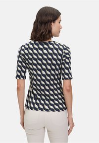 Marineblauw t-shirt met korte mouwen, voorzien van een golvend crème en groene print. Zacht materiaal, ronde halslijn en aansluitende snit. Draagt bij lichte broek.