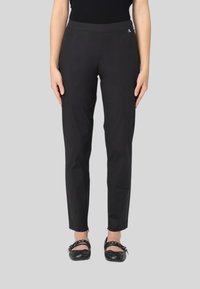 Pantaloni neri con una texture liscia, slim fit e una cintura comoda, abbinati a scarpe nere piatte con dettagli in catena.