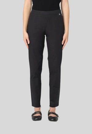 Pantaloni neri con una texture liscia, slim fit e una cintura comoda, abbinati a scarpe nere piatte con dettagli in catena.