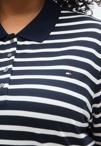 Μπλε και άσπρο ριγέ πόλο πουκάμισο με κουμπωτό άνοιγμα, γιακά και μικρό λογότυπο στ ο στήθος. Κατασκευασμένο από υφασμάτινη υφή.