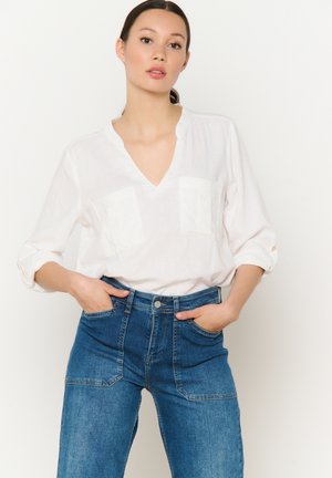 Camicia bianca leggera con scollo a V e due tasche sul petto, abbinata a jeans in denim blu a vita alta con una finitura texture.