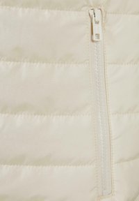 Helebeežist beež värvi paks jope, millel on horisontaalne tikandmustrit ja keskel valge tõmblukk. Pehme, sile kangas läikiva viimistlusega.