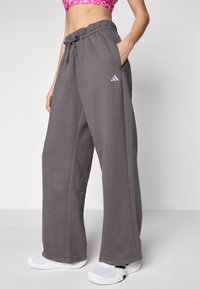 Sive hlače za sproščene trenutke, izdelane iz mehke tkanine, z elastičnim pasom in vrvico ter logotipom Adidas na levi nogi. Zasnova z širokimi hlačnicami.