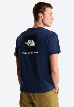 Camiseta de algodón azul marino con un gráfico cuadrado negro en la espalda que presenta el texto "THE NORTH FACE" y "NEVER STOP EXPLORING" en blanco.