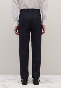 Pantalones de vestir azul marino con ajuste cónico, confeccionados en tela lisa; cuentan con dos bolsillos traseros con botones y un diseño limpio y a medida.