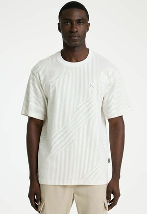 Man draagt beige cargobroek en een wit T-shirt met korte mouwen met dunne, schuine grijze strepen op een effen achtergrond.