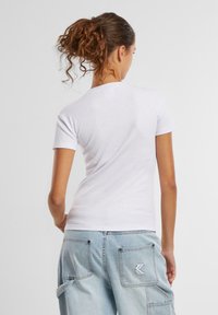 T-shirt blanche à manches courtes avec un design ajusté, texture côtelée et col rond, associée à un pantalon cargo bleu clair avec des écussons.