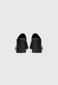 Zwarte high heels hebben een gladde afwerking met een ronde neus en robuuste ribbelige blokhakken, waarbij ze van achteren een strak ontwerp tonen.