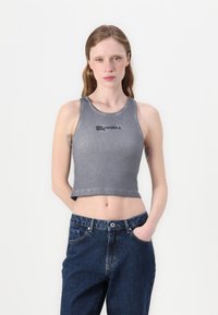 Grijze gecropte tanktop met geribbelde textuur en zwart "KARL LAGERFELD JEANS" logo aan de voorkant, gecombineerd met donkerblauwe spijkerbroek.