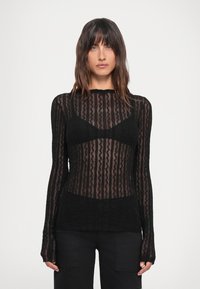 Maglietta nera a maniche lunghe con un design trasparente e testurizzato caratterizzato da motivi ondulati. La scollatura è rotonda e il tessuto ha una leggera lucentezza.