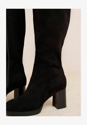 Schwarze Wildleder-Stiefel bis zum Knie mit einem stabilen Blockabsatz und einem seitlichen Reißverschluss, die eine glatte Textur und eine schlanke Silhouette aufweisen.