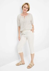 Blouse légère rayée beige avec un détail à nouer au col, assortie à un pantalon cropped crème et des sandales neutres.