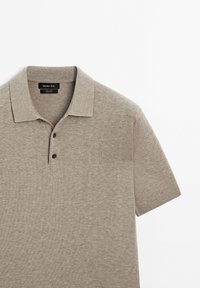 Polo beige à manches courtes avec deux boutons et un col plié, posé à plat sur un fond blanc.