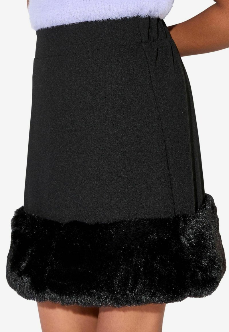 Jupe noire taille haute avec un large contour en fausse fourrure au bas, portée avec un haut blanc en matière douce.