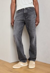 Jeans de mezclilla gris con un corte holgado, ligero desgaste y diseño clásico de cinco bolsillos, combinados con zapatillas beige claras.