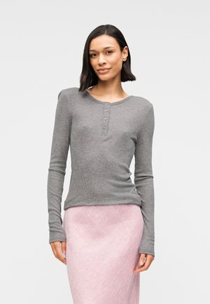 Haut henley gris à manches longues avec une texture côtelée, doté d'un col arrondi et d'une patte à quatre boutons, associé à une jupe rose texturée.