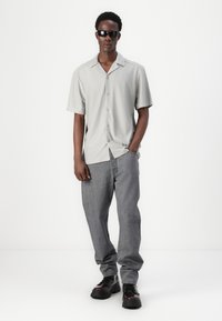 Lysegrå kortermet skjorte med knapper og fin ribbet tekstur, sammen med løse grå jeans og svarte snørebåndsstøvler. Svarte solbriller.