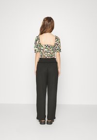 Top curto floral em preto com mangas bufantes e costas quadradas, combinado com calças largas de cintura alta em preto com um tecido texturizado.
