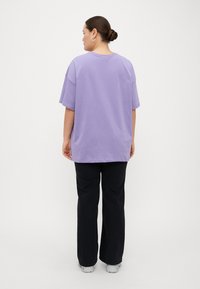 Una camiseta de corte holgado y de manga corta en algodón morado claro, combinada con pantalones negros. La camiseta tiene un escote redondeado y un corte recto.