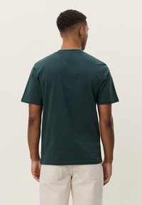 Zelena pamučna majica kratkih rukava, s okruglim izrezom i opuštenim krojem, s glatkom teksturom i minimalističkim dizajnom.