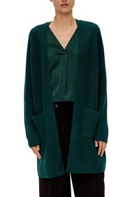 Lunga cardigan teal realizzata in tessuto a maglia testurizzata. Presenta un'apertura frontale, due tasche anteriormente e polsini a coste. Indossato sopra un top verde.