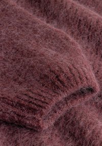 Miękka, puszysta dzianina w kolorze przygaszonego różu z prążkowanym mankietem, ukazująca teksturę i ciepło materiału.