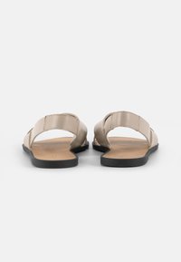 Beige sandaler med to brede stropper, en flad sort sål og en glat overflade. Minimalistisk design, åben bagside og ingen udsmykninger.