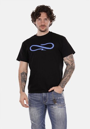 T-shirt in cotone nero con una grafica di un simbolo di infinito blu sul petto, abbinato a jeans chiari strappati.