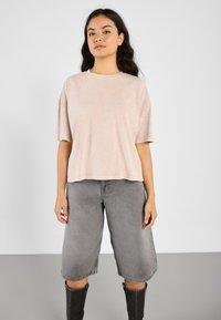 Lys rosa t-skjorte med korte ermer og avslappet passform, kombinert med grå denimshorts til kneet og svarte støvler til kneet.