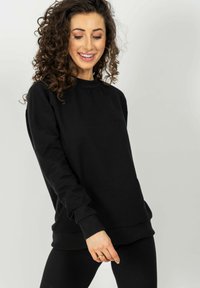 Czarna bluza z miękkiego materiału z prążkowanymi akcentami. Posiada okrągły dekolt i małe, wytłoczone logo na piersi. Wygodny krój.