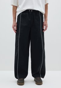 Zwarte cargobroek met een losse pasvorm, voorzien van witte zijstrepen, een elastische tailleband met trekkoord en steekzakken aan de voorkant.