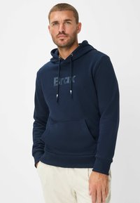Felpa con cappuccio di colore blu navy in morbido materiale, con tasca a marsupio frontale e stampa del logo in una tonalità più scura sul petto.