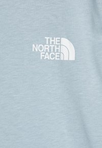 Hellblaues Baumwoll-T-Shirt mit einem weißen Logo von The North Face, das sich auf der linken Brustseite befindet. Neben der sanften Textur zeichnet es sich durch ein minimalistisches Design aus.