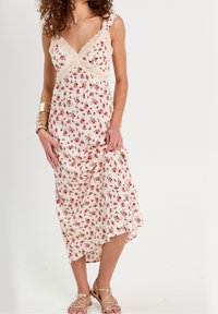 Robe midi florale en crème, dotée d'une délicate dentelle au niveau du col et de fines bretelles, avec un tissu fluide et léger et un ourlet asymétrique.