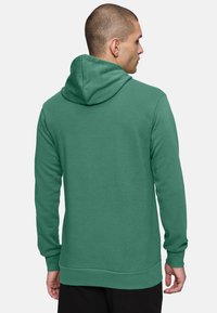 Felpa verde con cappuccio, dal tessuto morbido, con polsini e orlo elasticizzati. Design a vestibilità rilassata, vista dal retro, che mostra il cappuccio.