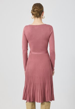 Langermet kjole i støvete rosa materiale; tettsittende liv med plisserte skjørtedetaljer, glatt tekstur og knelengde.
