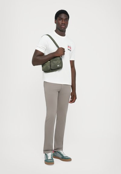 Grön nylon crossbody-väska med två framfickor, bärs med en vit t-shirt och ljusgrå byxor, kombinerad med gröna och grå sneakers.