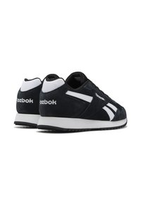 Baskets en suede noires avec des accents blancs et un logo. Design bas avec une semelle en caoutchouc noir et blanc, présentant une surface texturée et des lignes épurées.