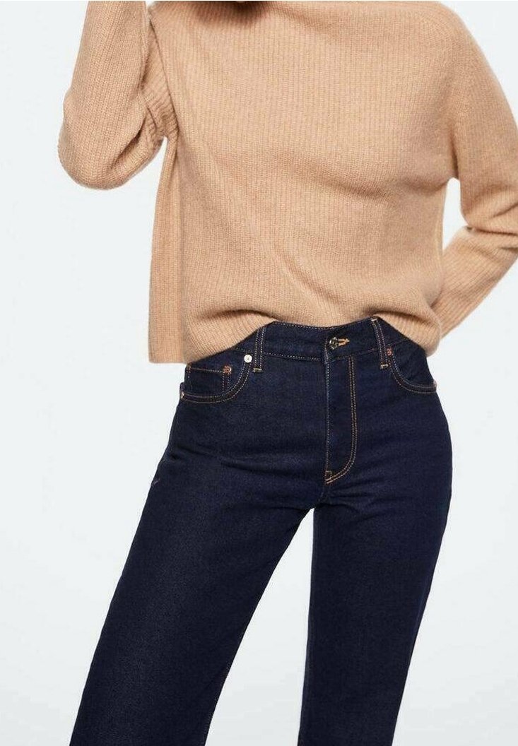 Pull en maille beige associé à un jean bleu foncé taille haute avec coutures orange et poches avant.
