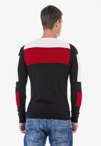 Schwarzer Pullover mit horizontalen roten und weißen Streifen; gerippte Textur an Schultern und Ärmeln; taillierte Passform; kombiniert mit blauen Jeans.