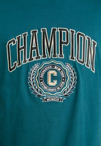 T-shirt de algodão verde-água com a palavra "CHAMPION" em negrito preto e um logótipo circular bordado com detalhes de louros e "Rochester, Nova Iorque."