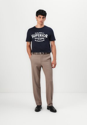 Marineshirt mit weißem Druck, kombiniert mit beigen Hosen. Die Hosen sind maßgeschneidert, haben eine glatte Textur und ein einfaches Design. Schwarze Schuhe runden das Outfit ab.