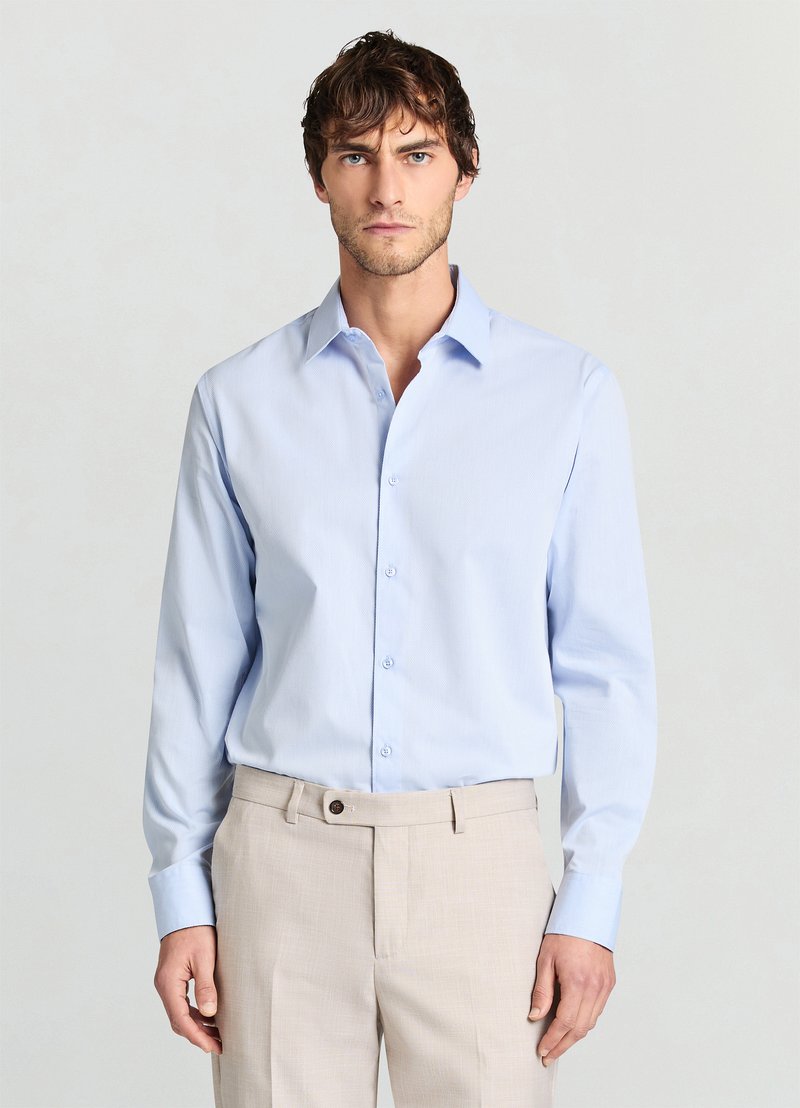 Camicia celeste chiaro con colletto strutturato e maniche lunghe, tessuto strutturato, abbinata a pantaloni beige chiaro su misura.