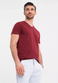 Burgundské bavlněné tričko s výstřihem do V a krátkým rukávem ve spojení se světle modrými kalhotami. Tkanina vypadá hladce a má volný střih.