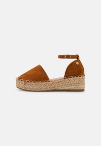 Brown suede espadrille with an ankle strap, featuring a jute-wrapped wedge sole and stitched detailing along the edge.