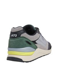Sneaker da uomo con una tomaia in suede grigio, accenti verdi e dettagli in pelle nera. Presenta una suola gialla e la scritta "1973" sul tallone.